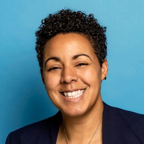 Smiling person with short curly hair against a blue background.