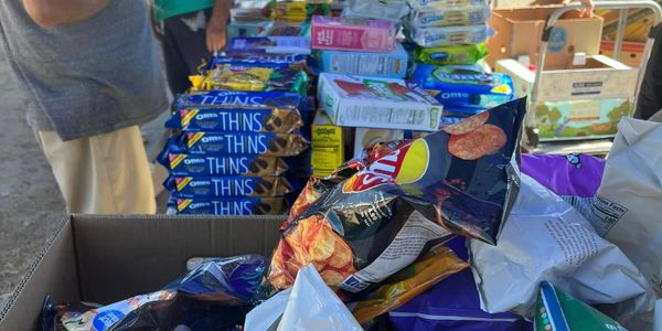 Table filled with assorted snack packages including chips and cookies outdoors.
