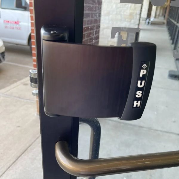 Push to exit paddle on a commercial storefront door in dark bronze. Meets life safety code rules