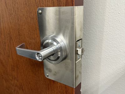 Locking commercial door lever with a protective door wrap on a wooden door in an office building