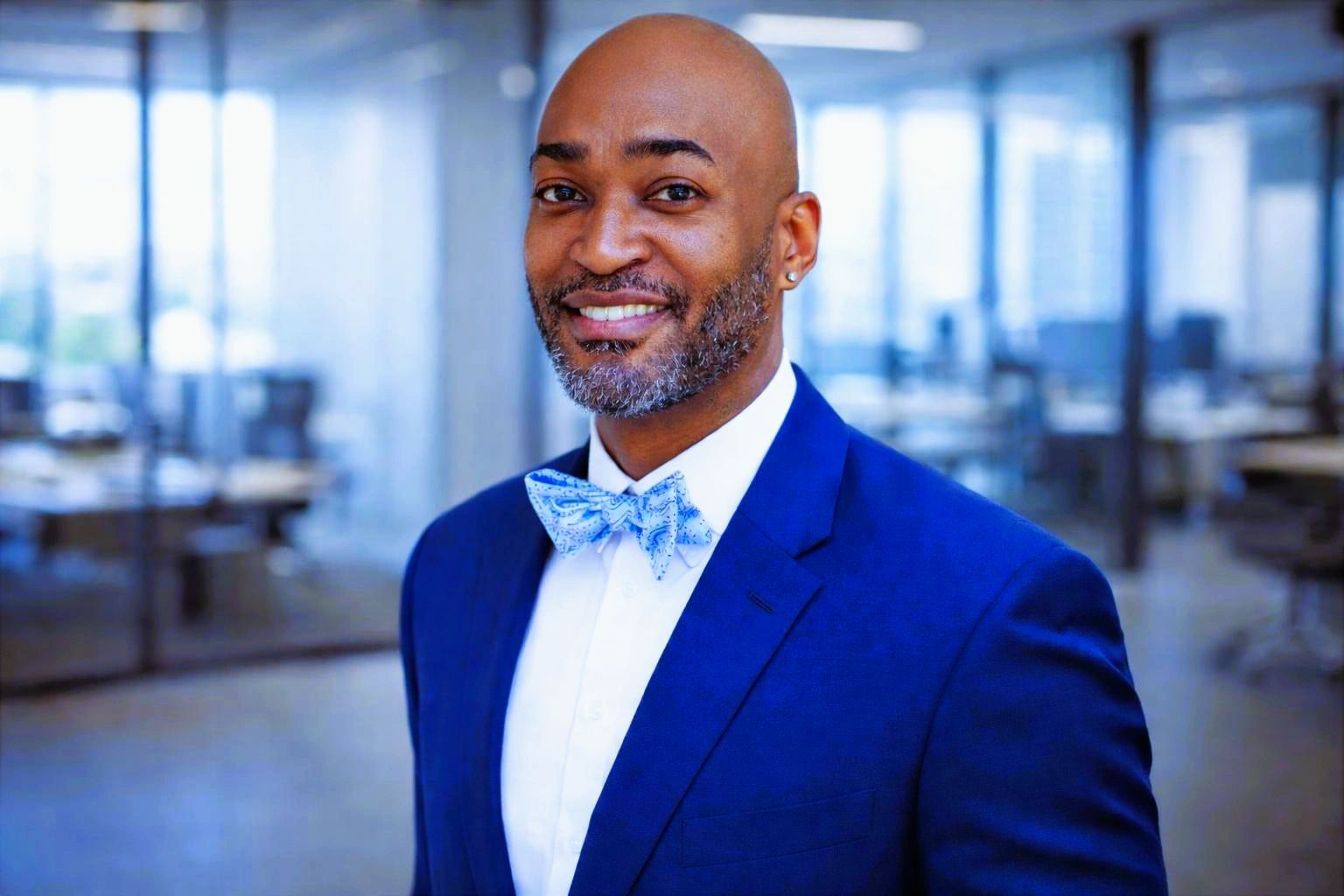 Smiling man in a blue suit and bow tie in an office setting.