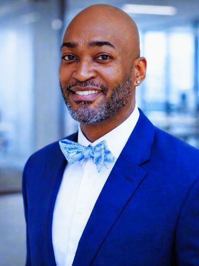 A smiling man in a blue suit and patterned bow tie.