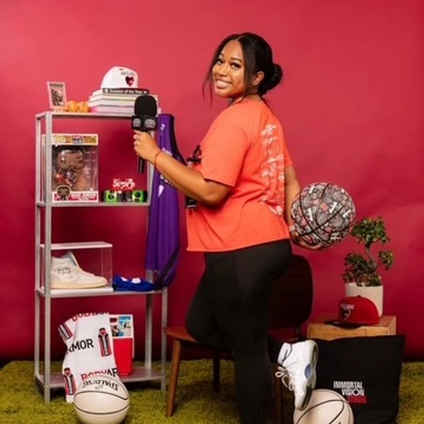 Woman in orange shirt holding microphone and basketball in a vibrant sports-themed room.