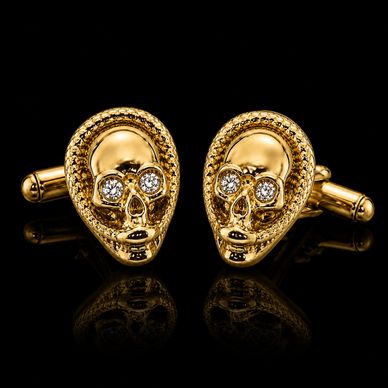 Gold skull cufflinks with diamond eyes on black background.