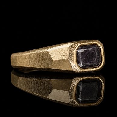Gold ring with a dark gemstone reflecting on a black surface.