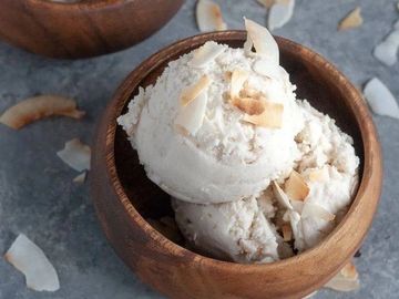 Scoops of coconut ice cream in wooden bowls garnished with toasted coconut flakes.