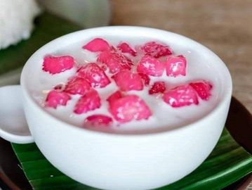 Cup of colorful dessert with pink toppings in milky liquid.