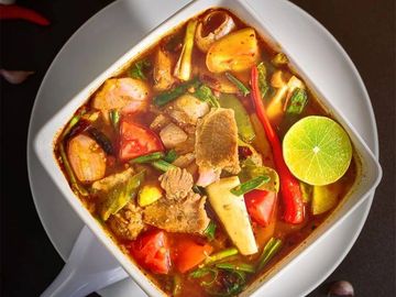 Spicy Thai soup with lime and fresh vegetables in a white bowl.