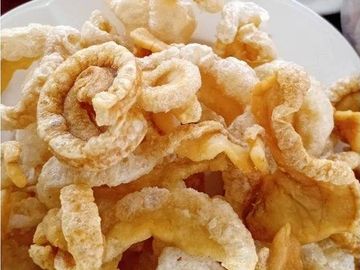 Crispy pork rinds served on a white plate with fresh herbs.