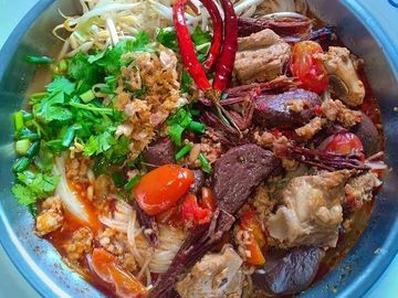 A vibrant bowl of spicy noodle soup with fresh herbs and chili peppers.