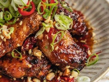 Spicy glazed chicken wings topped with sliced green onions and red chili peppers.