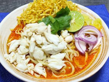 A bowl of spicy crab noodle soup garnished with lime, onions, and cilantro.