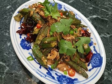 Spicy fried okra garnished with cilantro and red chilies on a decorative plate.