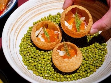 Three crispy pani puris filled with fish roe and herbs on a bed of green lentils.