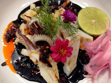 Grilled squid with black sauce, lime, pickled onions, and edible flowers.