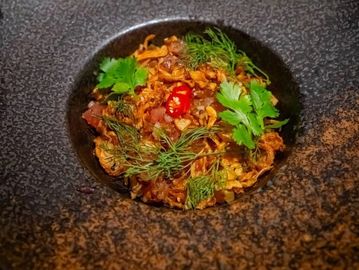 Gourmet dish garnished with herbs and chili in a textured bowl.