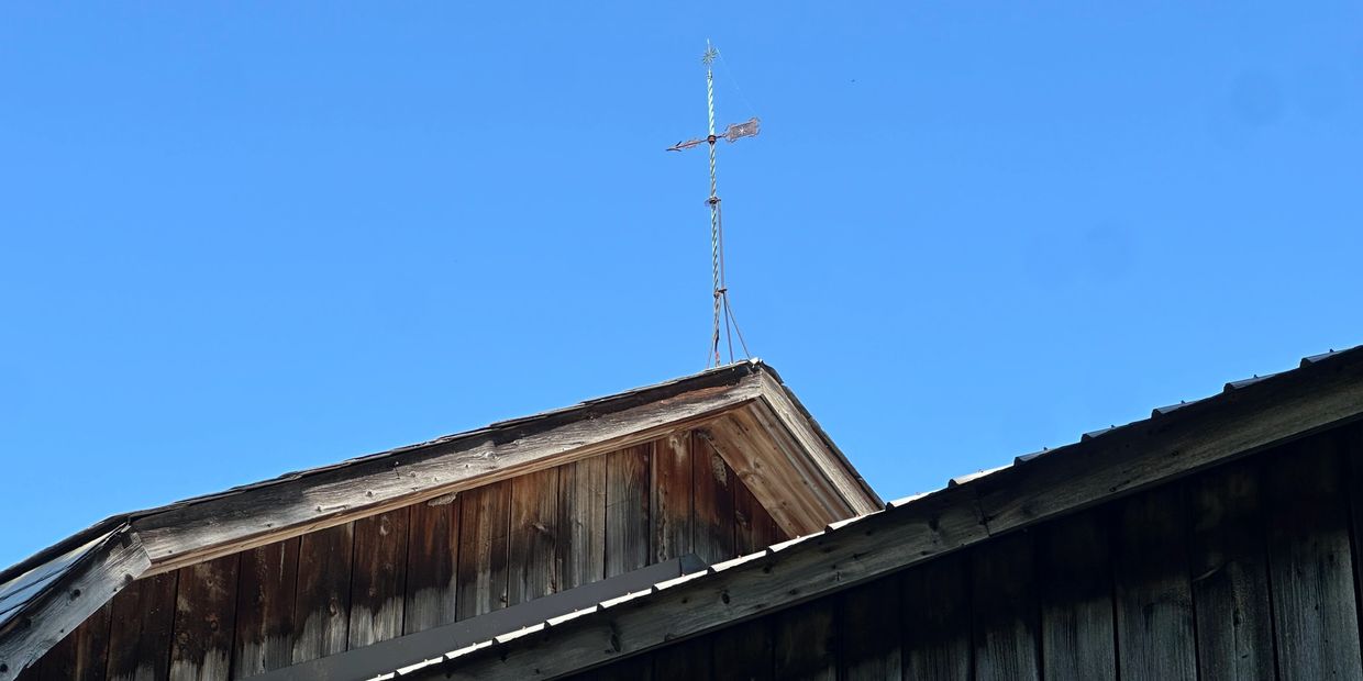 Weather vane on an old wooden building against a blue sky.