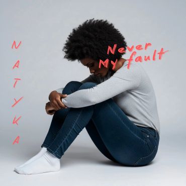 Woman sitting curled up, text says 'Never My Fault' and 'Natyka'.