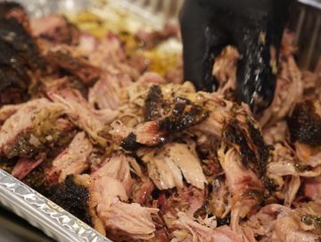 Gloved hand shredding smoked barbecue pork in a tray.