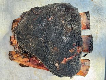 Burnt ribs with a heavily charred surface on a metal tray.