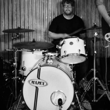 Man playing a Mapex drum set in a black-and-white photo.