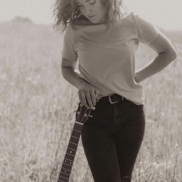 Woman standing in a field with a guitar.