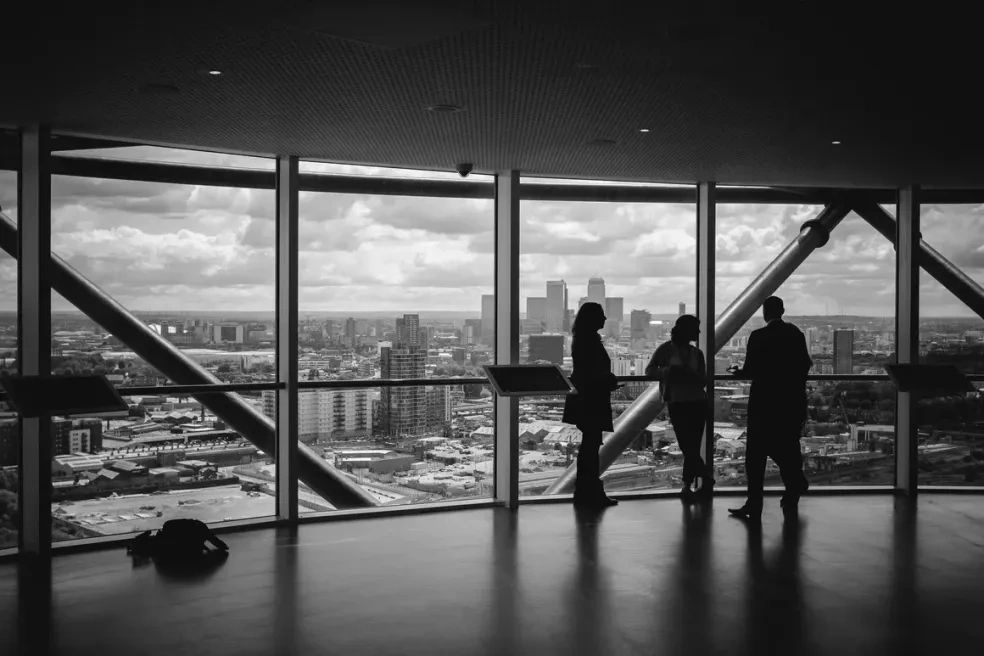 Three people silhouetted against large windows overlooking a cityscape.