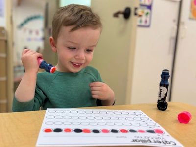 A young boy happily playing with a dot marker on a worksheet.