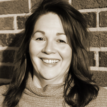 Smiling woman with long hair in front of a brick wall.