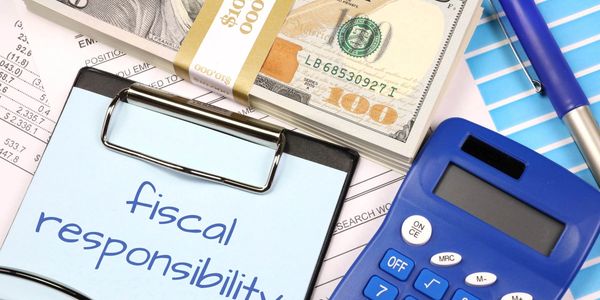 Clipboard with 'fiscal responsibility' note, money, calculator, and pen on financial documents.