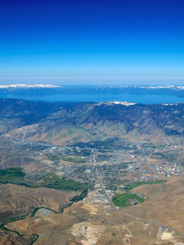 Aerial view of a town surrounded by mountains and a large lake under a clear blue sky.