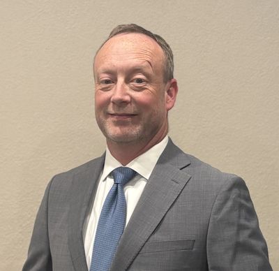 Confident man in a gray suit and blue tie smiling slightly.