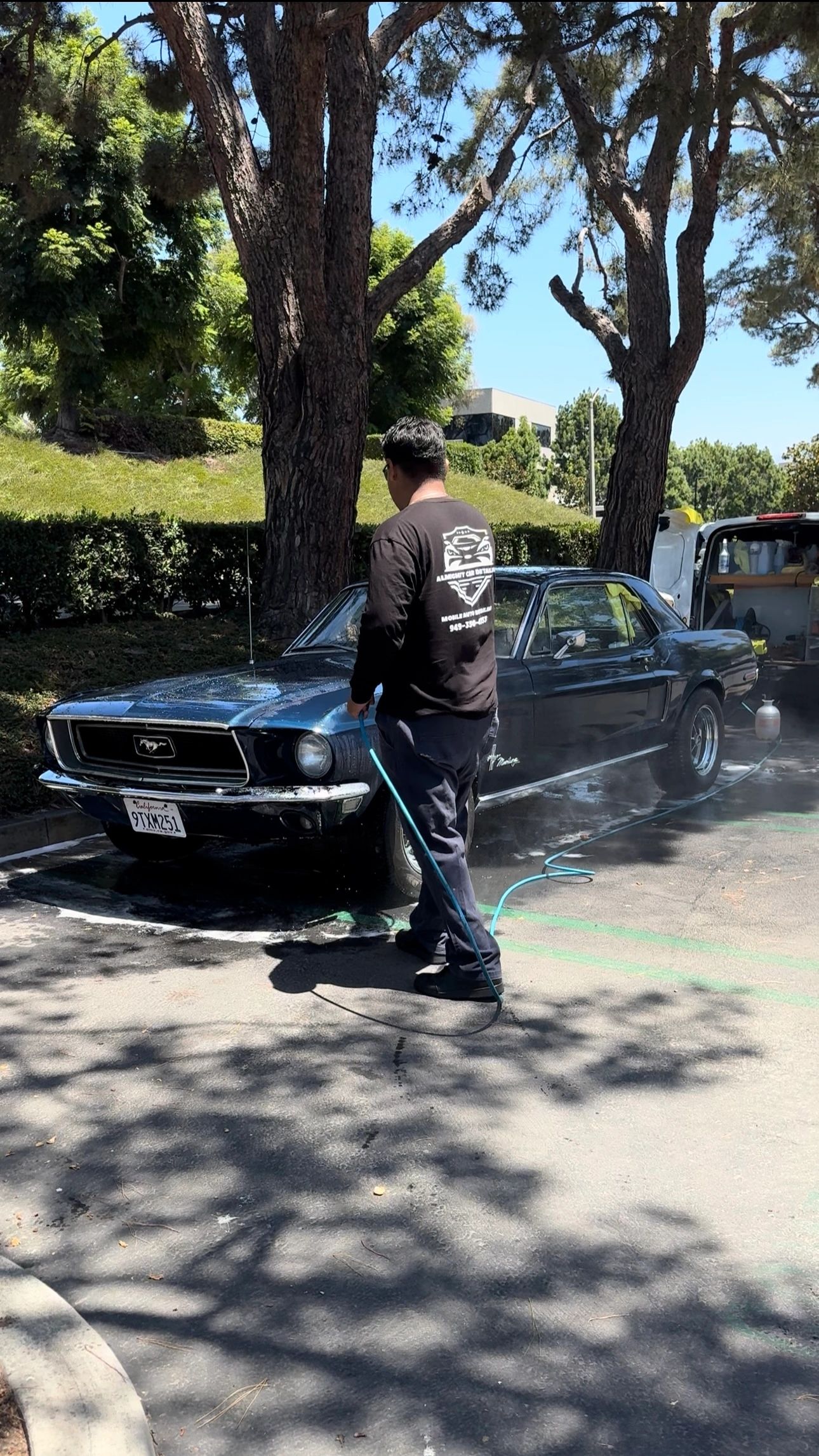 Man washing a classic Ford Mustang outside.