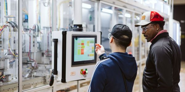 Two men operating a touchscreen control panel in a manufacturing facility.