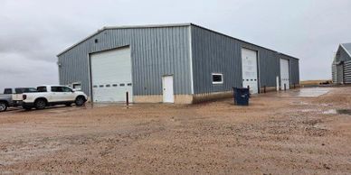 A gray metal industrial building with trucks parked outside on a muddy day.