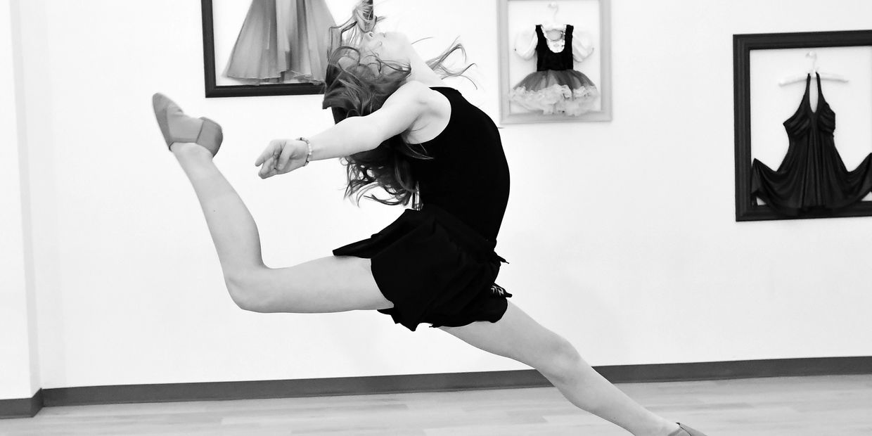 young irl leaping and dancing in the air inside a dance studio.