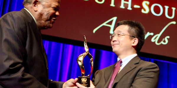 Two men exchanging a golden award on stage at an event.