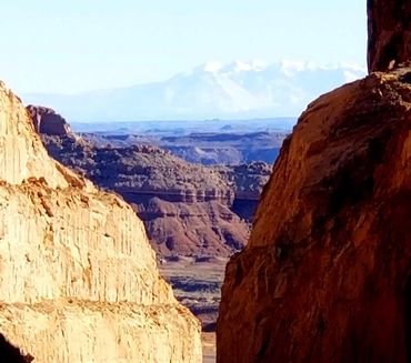 Sunlit canyon walls frame a distant mountain landscape under a clear blue sky.