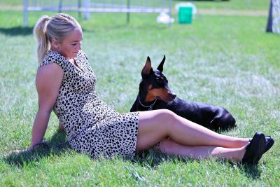 Woman sitting on grass with a Doberman dog.