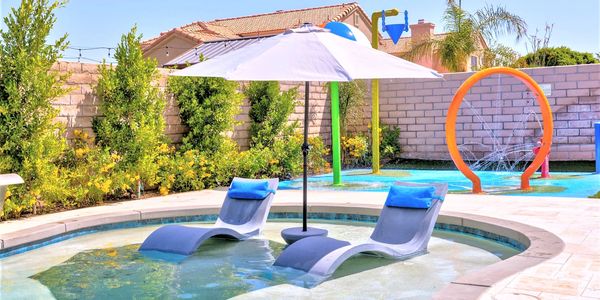 Poolside lounge chairs with umbrella and nearby water play area.