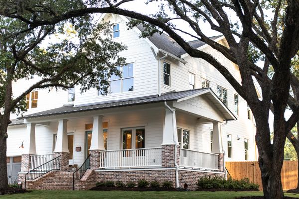 Large white house with wraparound porch and big trees.