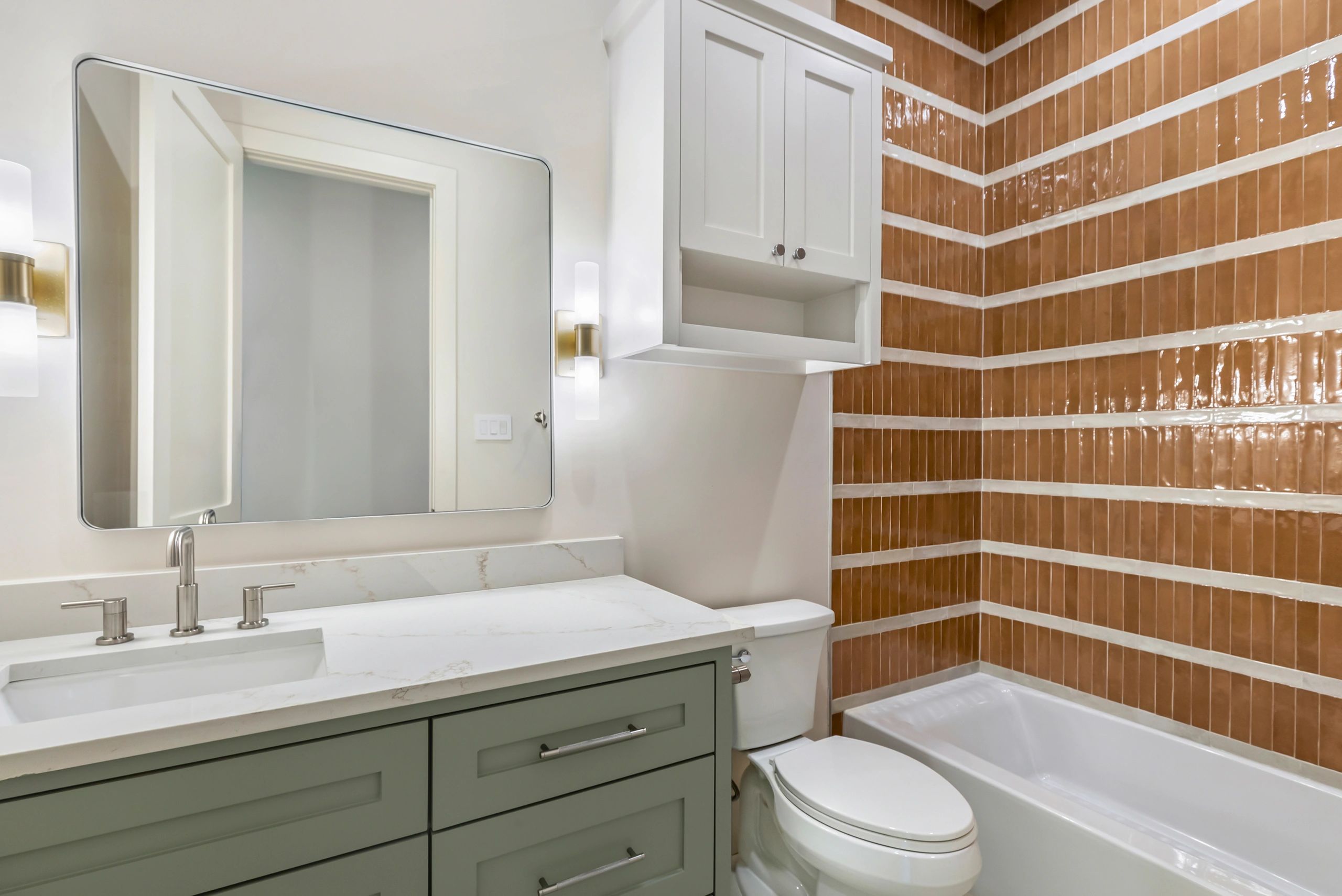 Modern bathroom with green vanity, white countertop, and brown tiled shower walls.