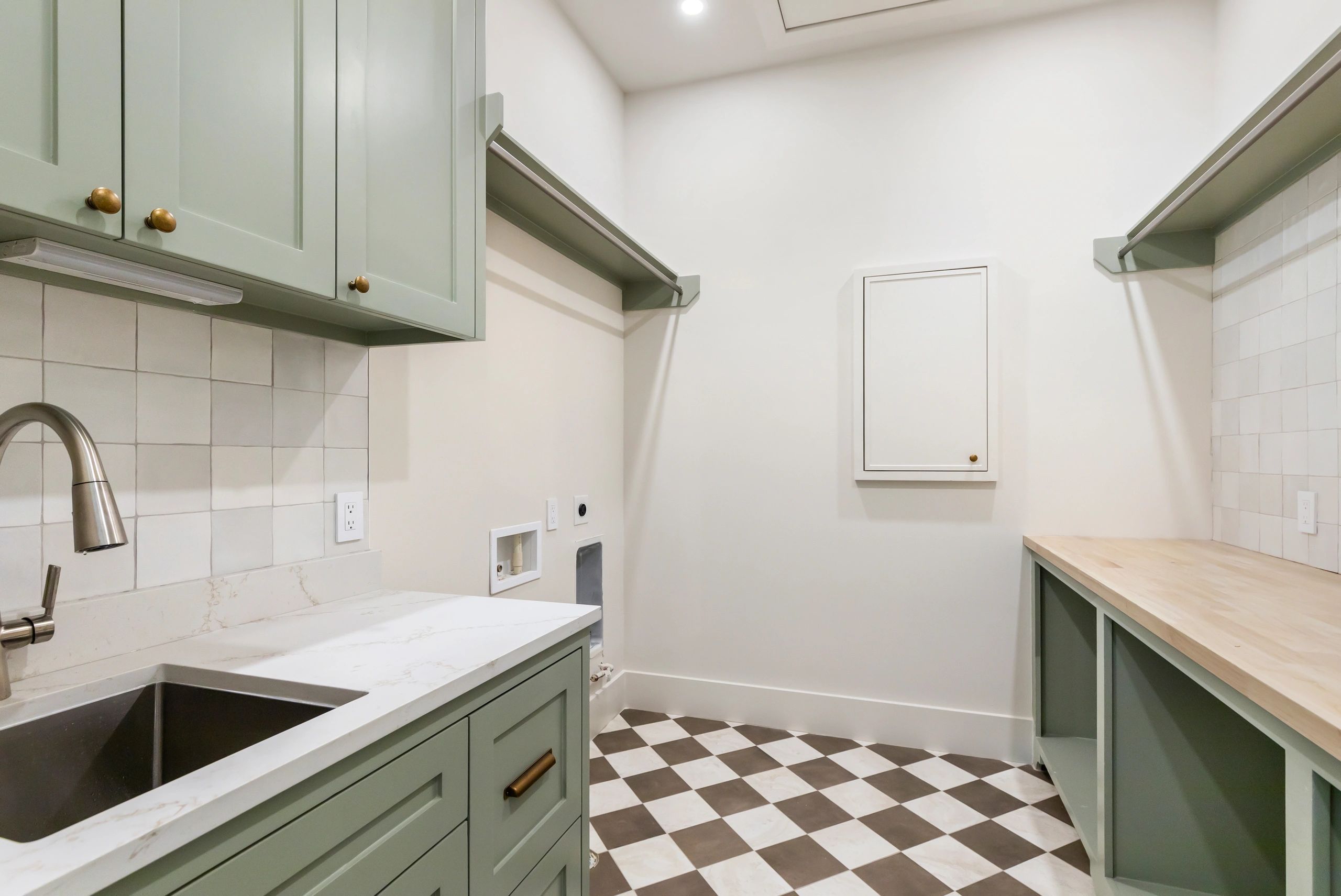 Modern laundry room with green cabinets and checkered floor tiles.
