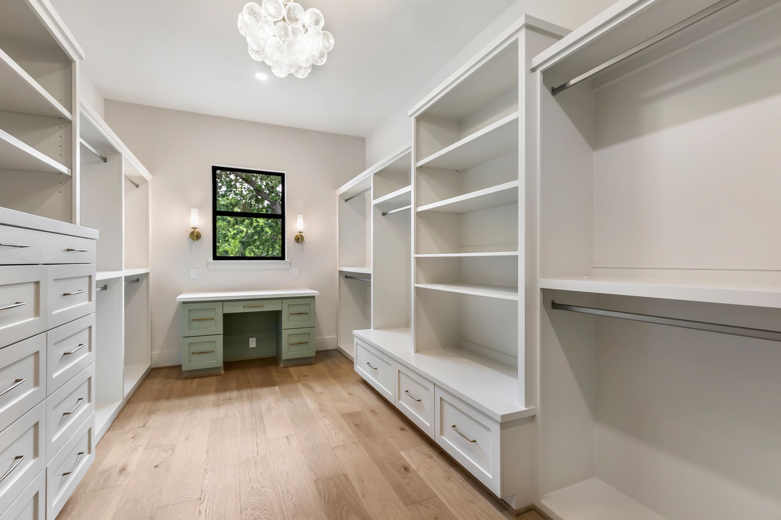 Spacious walk-in closet with white shelves and green desk under window.