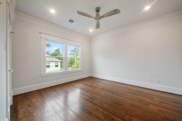 Empty room with wooden floors and ceiling fan under bright lights.