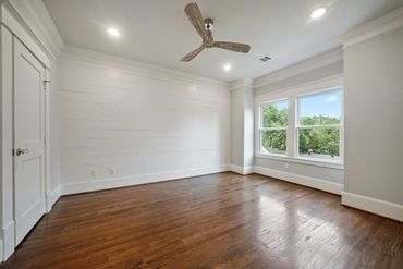 Empty room with wooden floor and large window letting in natural light.