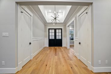 Bright hallway with black double doors and wooden floor.