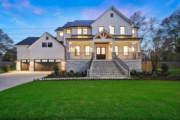 Modern farmhouse with large porch and spacious garage at dusk.