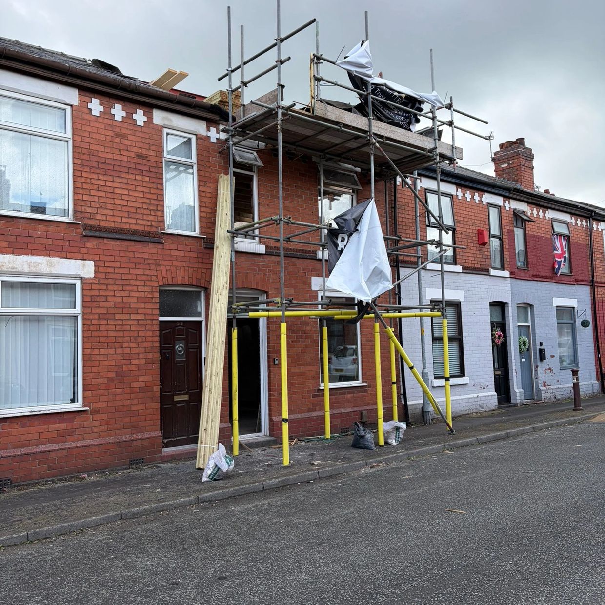 Scaffolding set up outside a brick terraced house under renovation on a cloudy day.