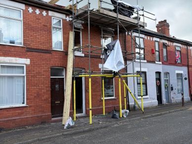 Scaffolding set up outside a brick terraced house under renovation on a cloudy day.